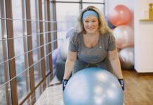 Kobieta ćwicząca na piłce fitness w grupowej sali treningowej