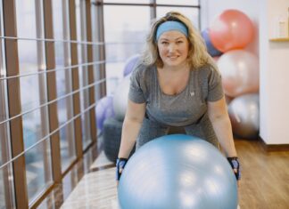 Kobieta ćwicząca na piłce fitness w grupowej sali treningowej
